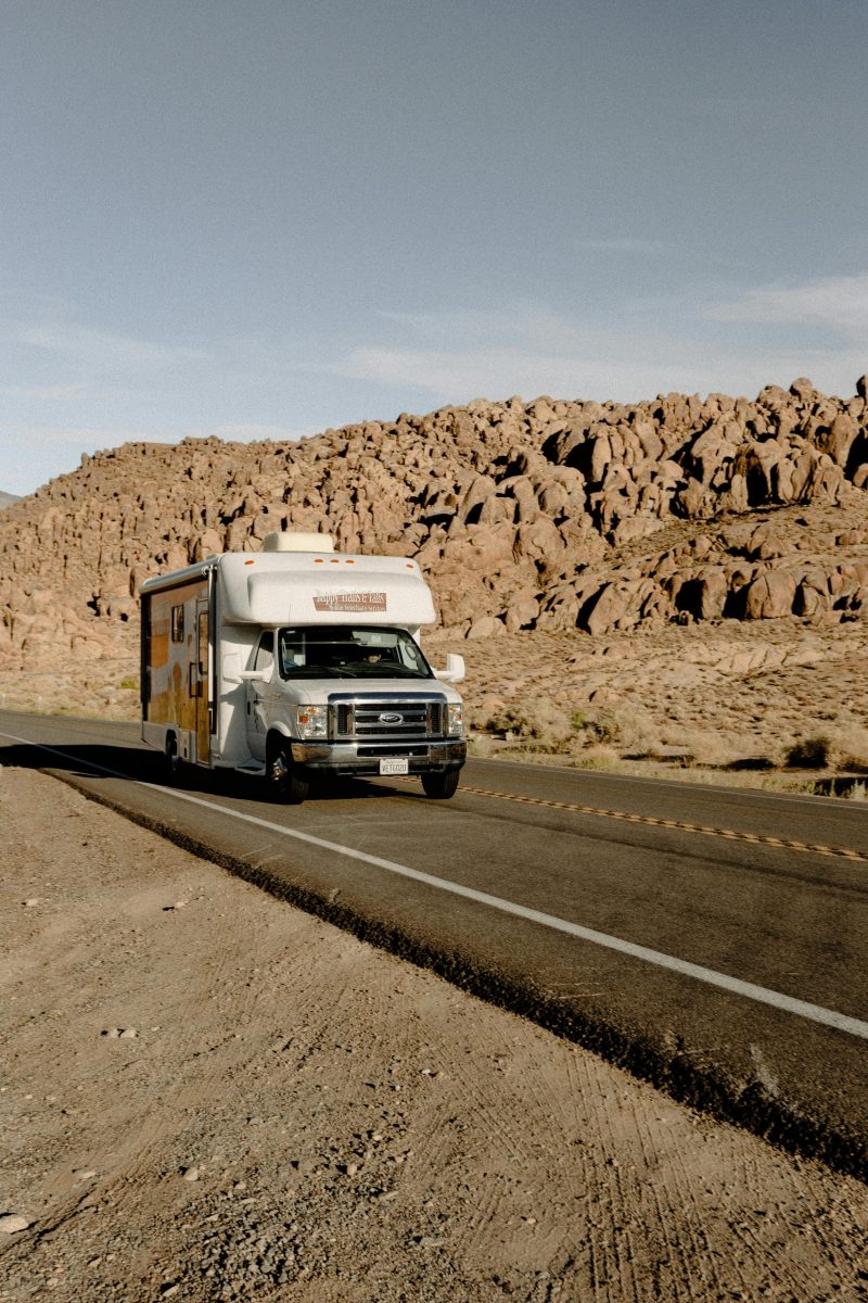 RV driving through a scenic desert highway with rocky mountains under a clear sky.