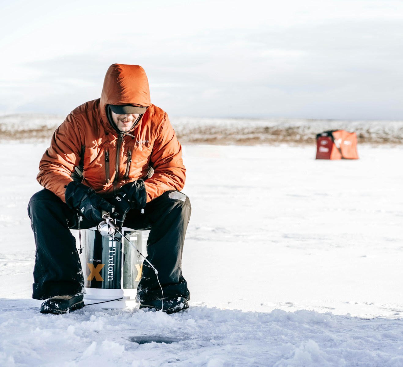 A man in brown jacket and black pants ice fishing