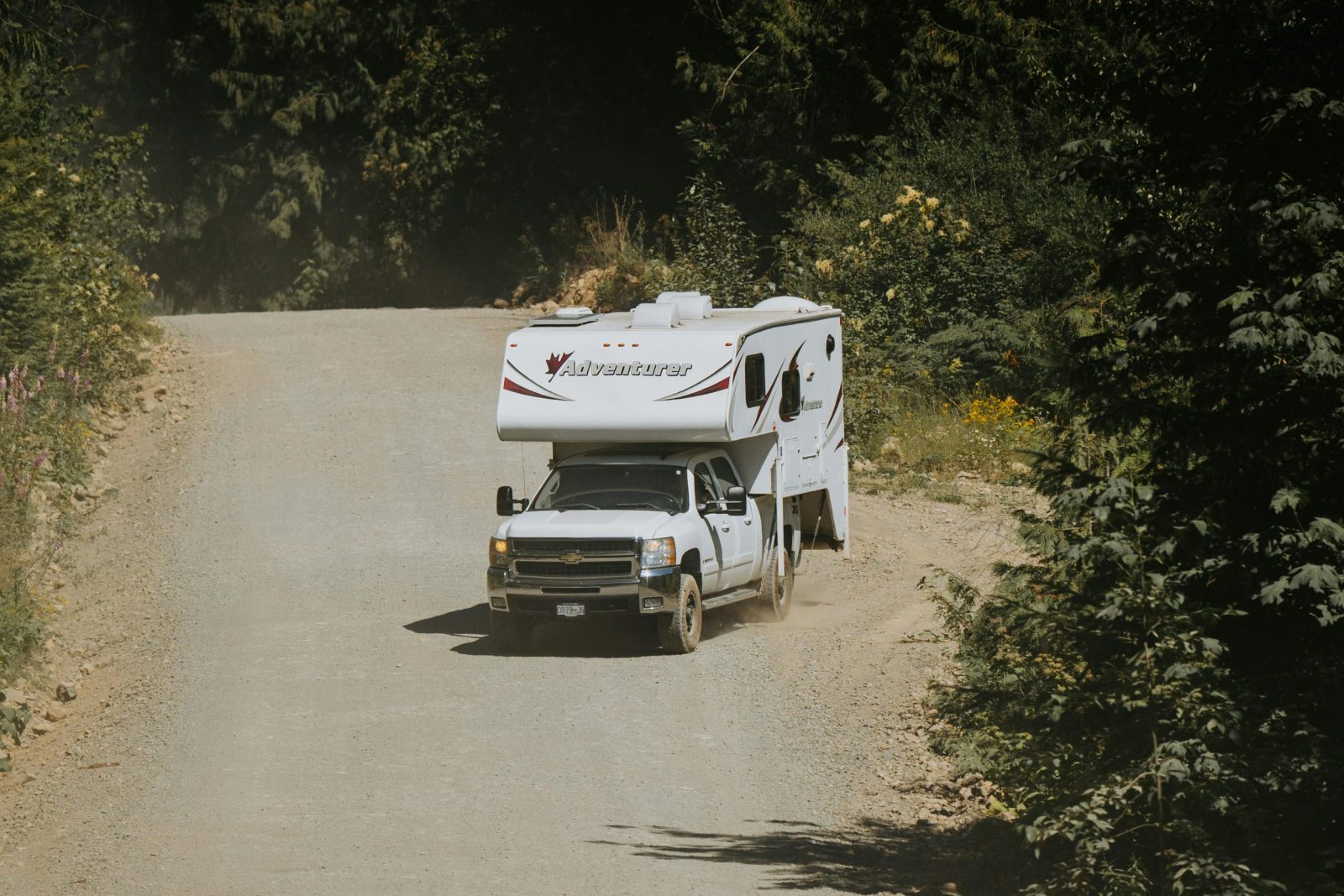 A white camper truck navigates a winding dirt road in a lush, forested area, perfect for adventure travel.