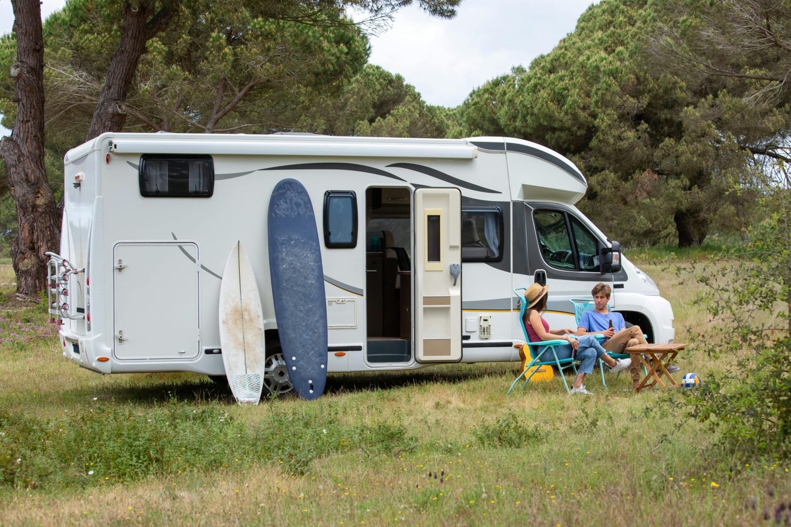 A Couple Relaxes Outside their RV with Surfboards.