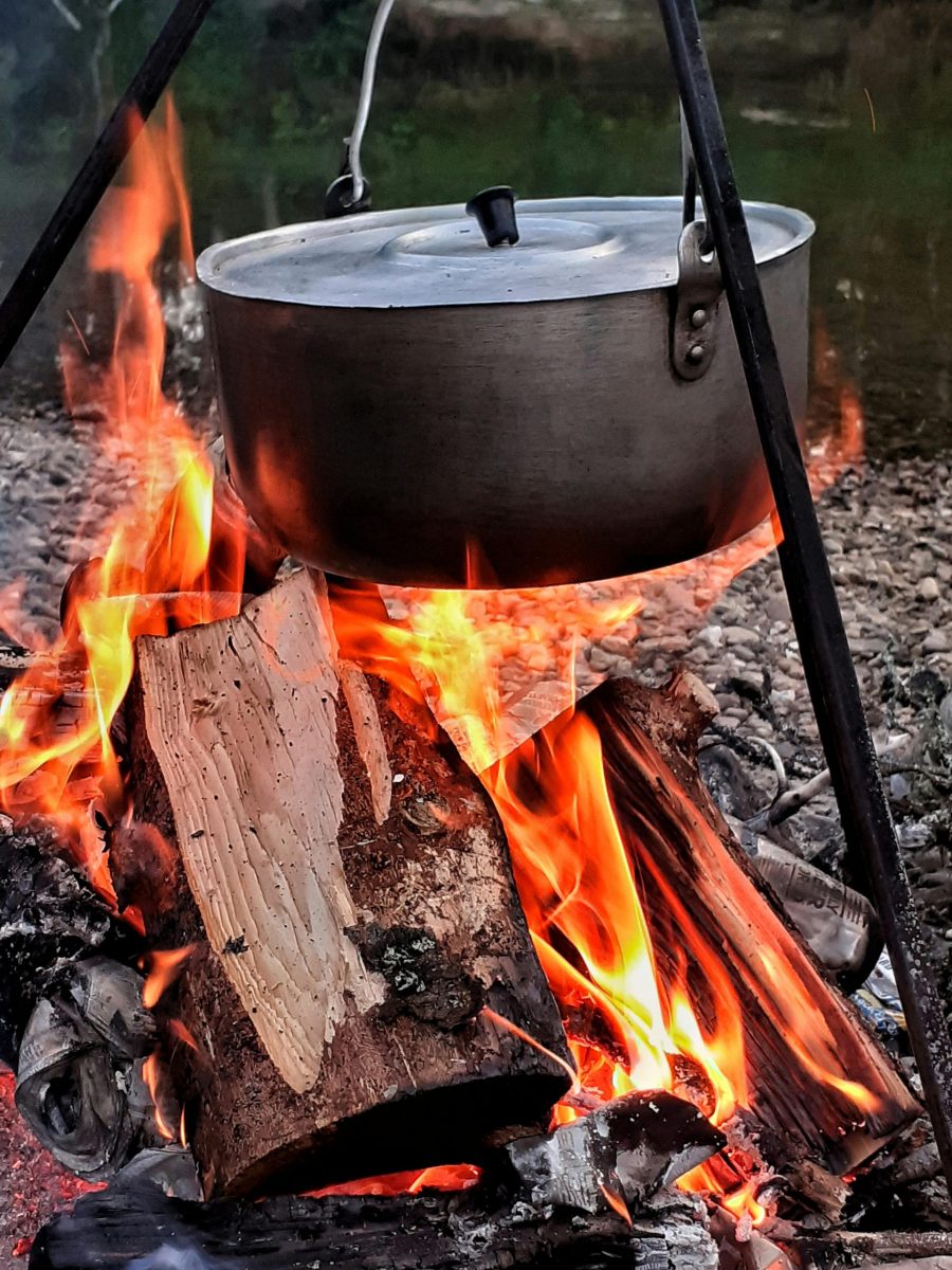 A metal pot hangs over a vibrant campfire in the wilderness, perfect for outdoor cooking.