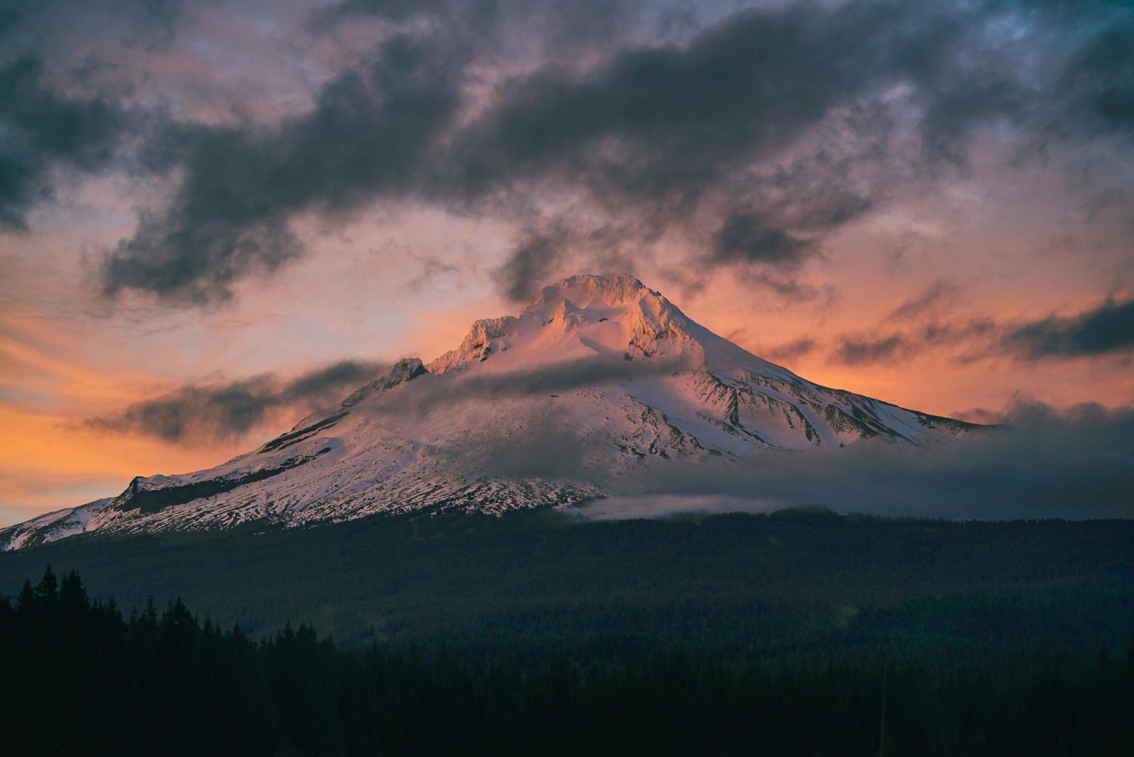 Captivating view of snow-capped Mount Hood surrounded by vibrant sunset skies and dramatic clouds.