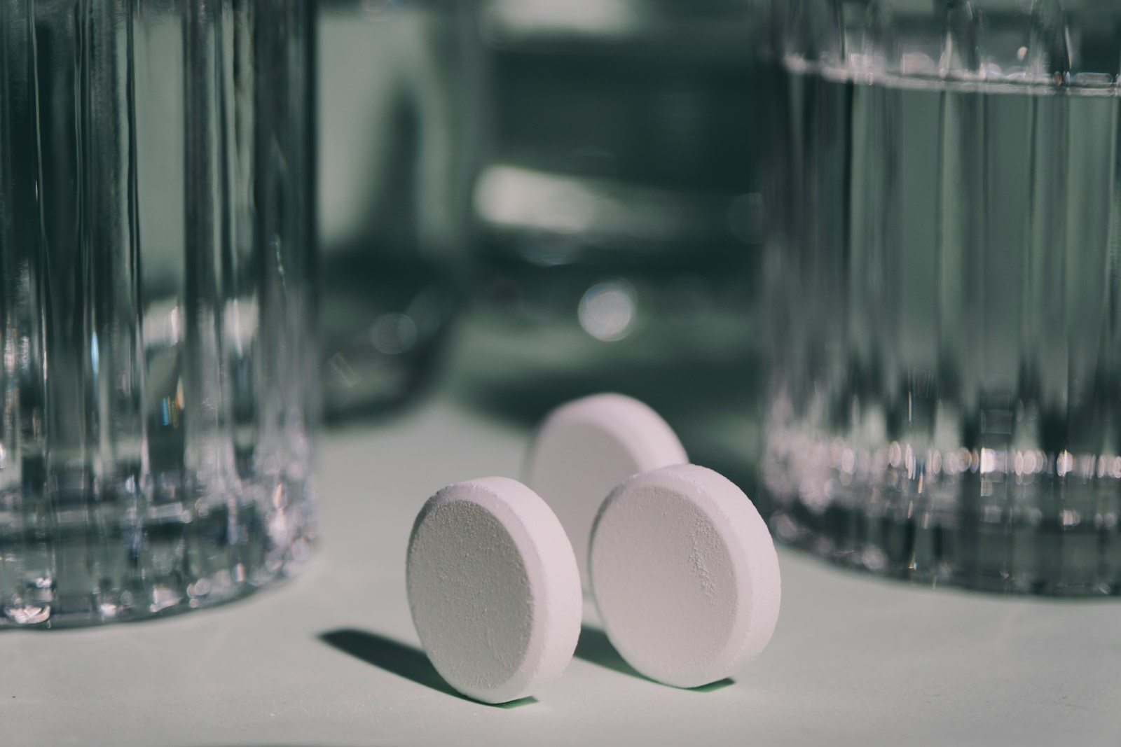 Three pills sitting on top of a table next to a glass of water