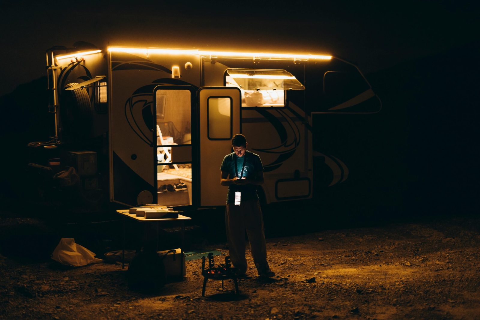 A night scene featuring an illuminated caravan with a person outside, set in a desert setting.