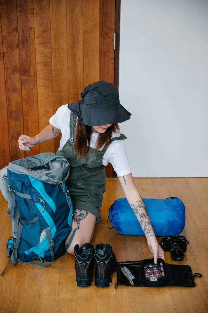 Woman preparing gear for hiking with backpack and boots on wooden floor.