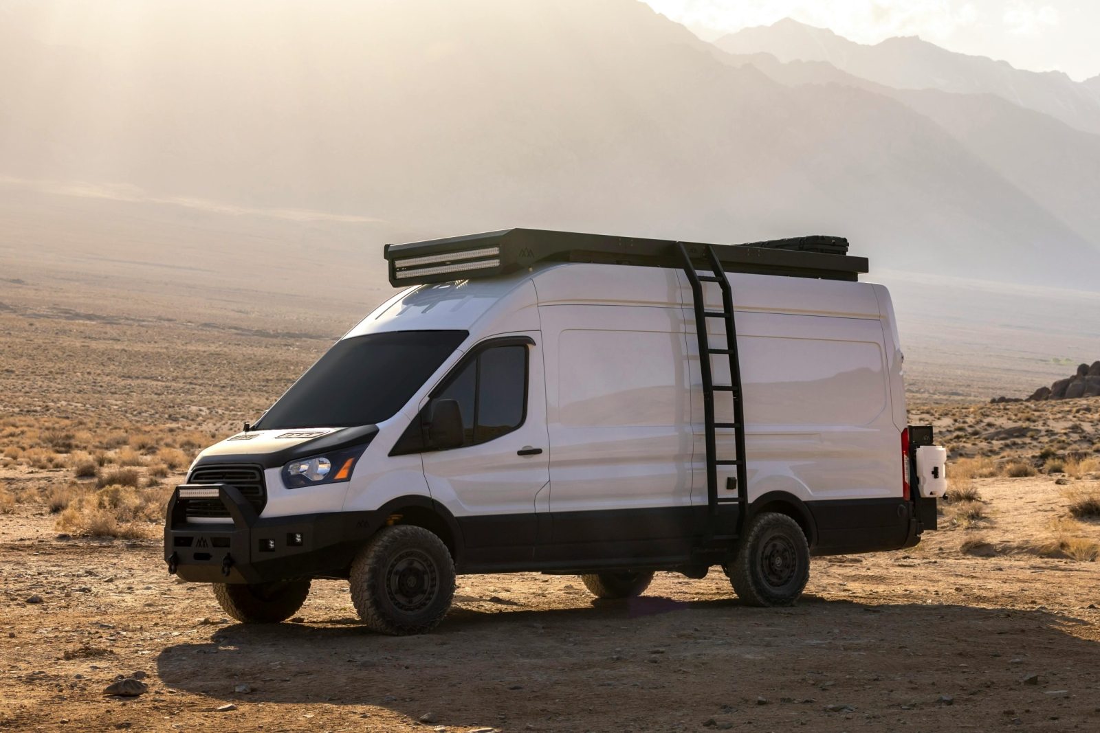 White camper van parked in a vast desert landscape under a clear daytime sky.