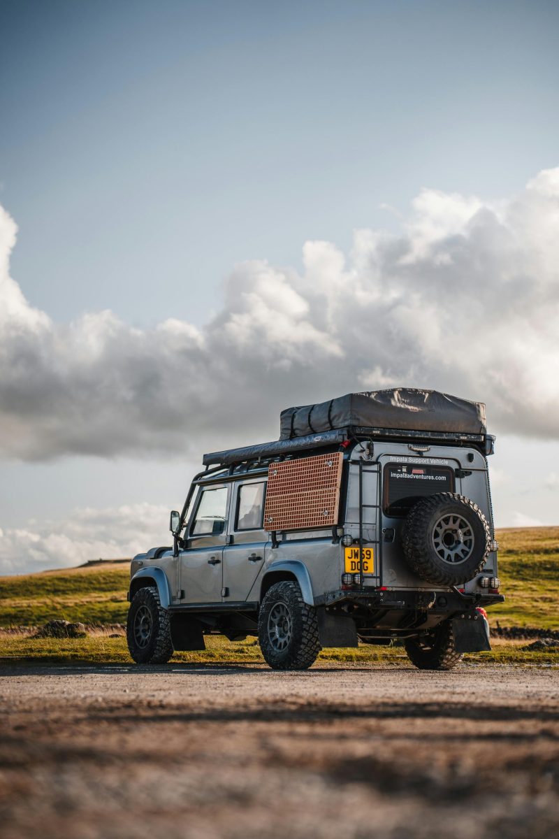 A Land Rover Defender parked on a scenic route under dramatic clouds.