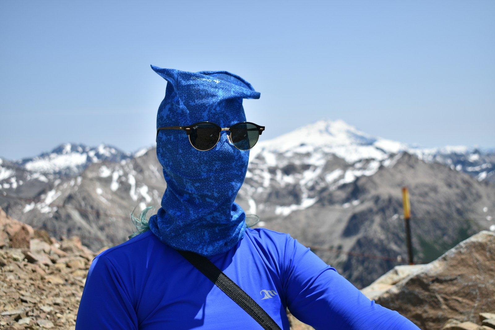 A person in blue jacket wearing black sunglasses and blue scarf
