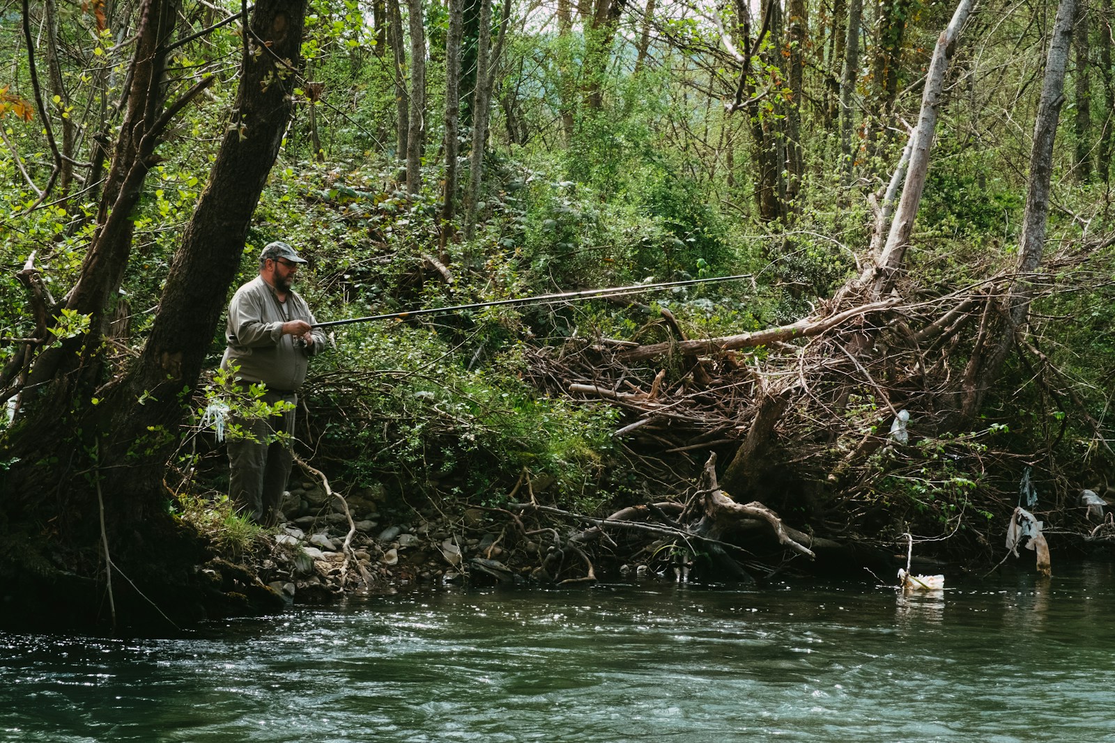 A man in white shirt and brown pants sitting on brown tree log on river