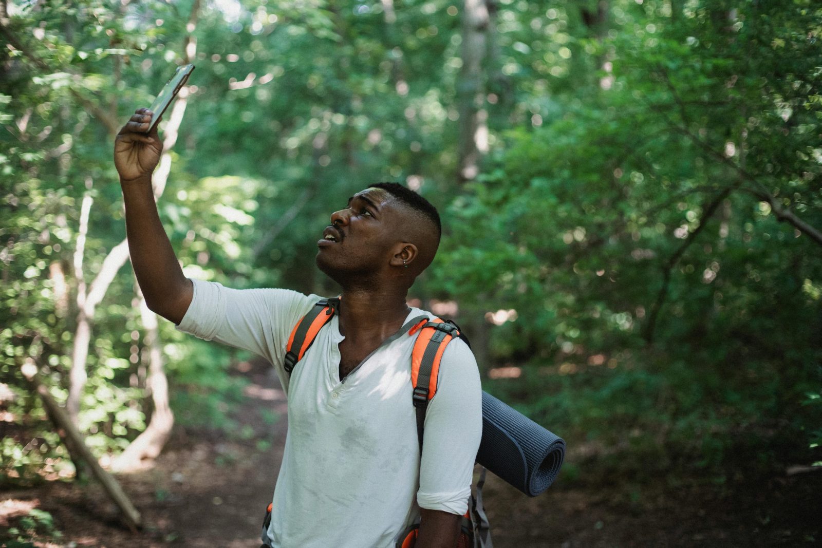 Male with backpack standing in forest and holding mobile phone while catching GPS signal during hike.