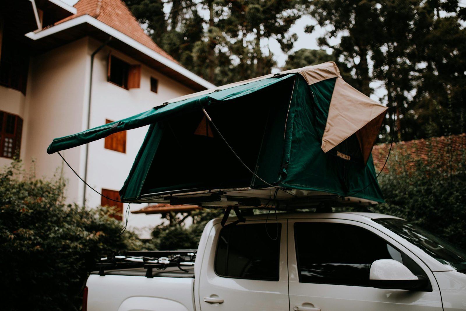 A rooftop camping tent set up on a white pickup truck parked outdoors near a house.