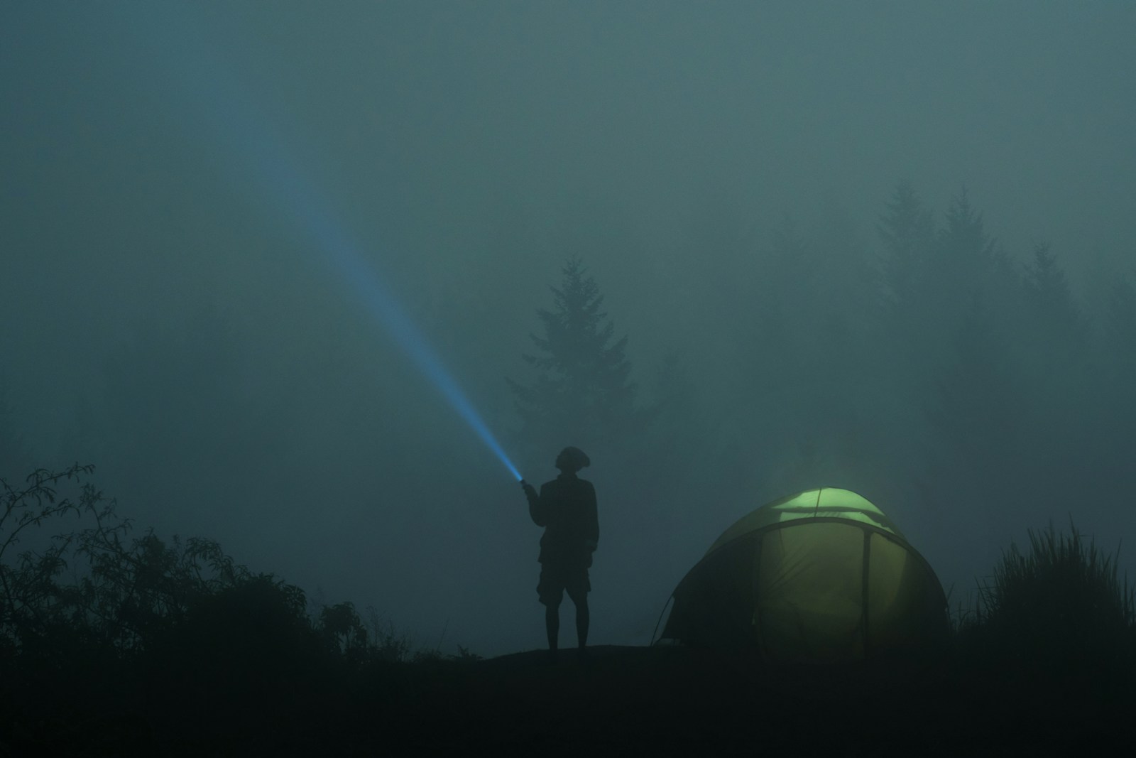 A person standing near dome tent while holding flashlight