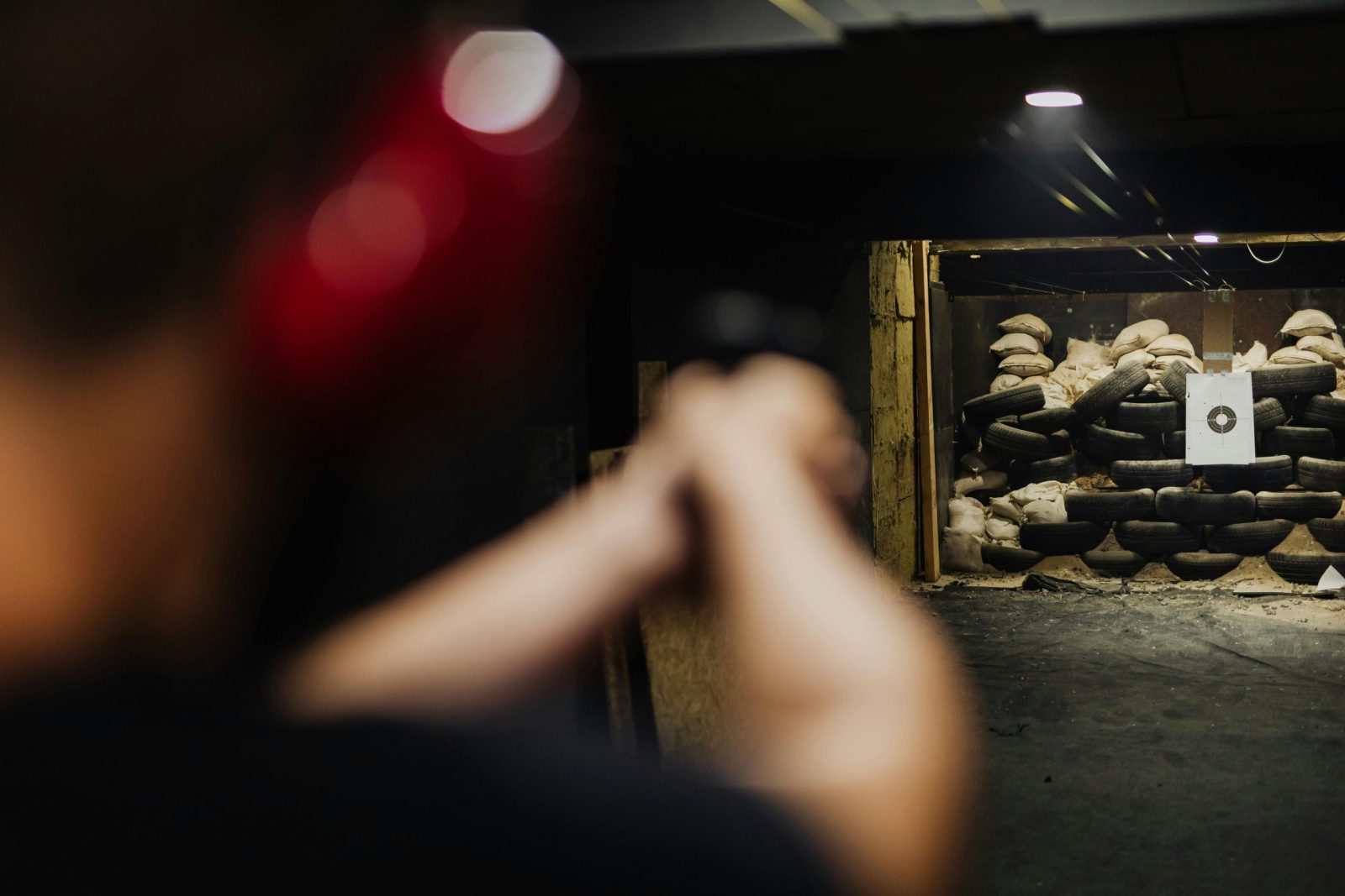 A person at an indoor shooting range aims at a stacked tire target.