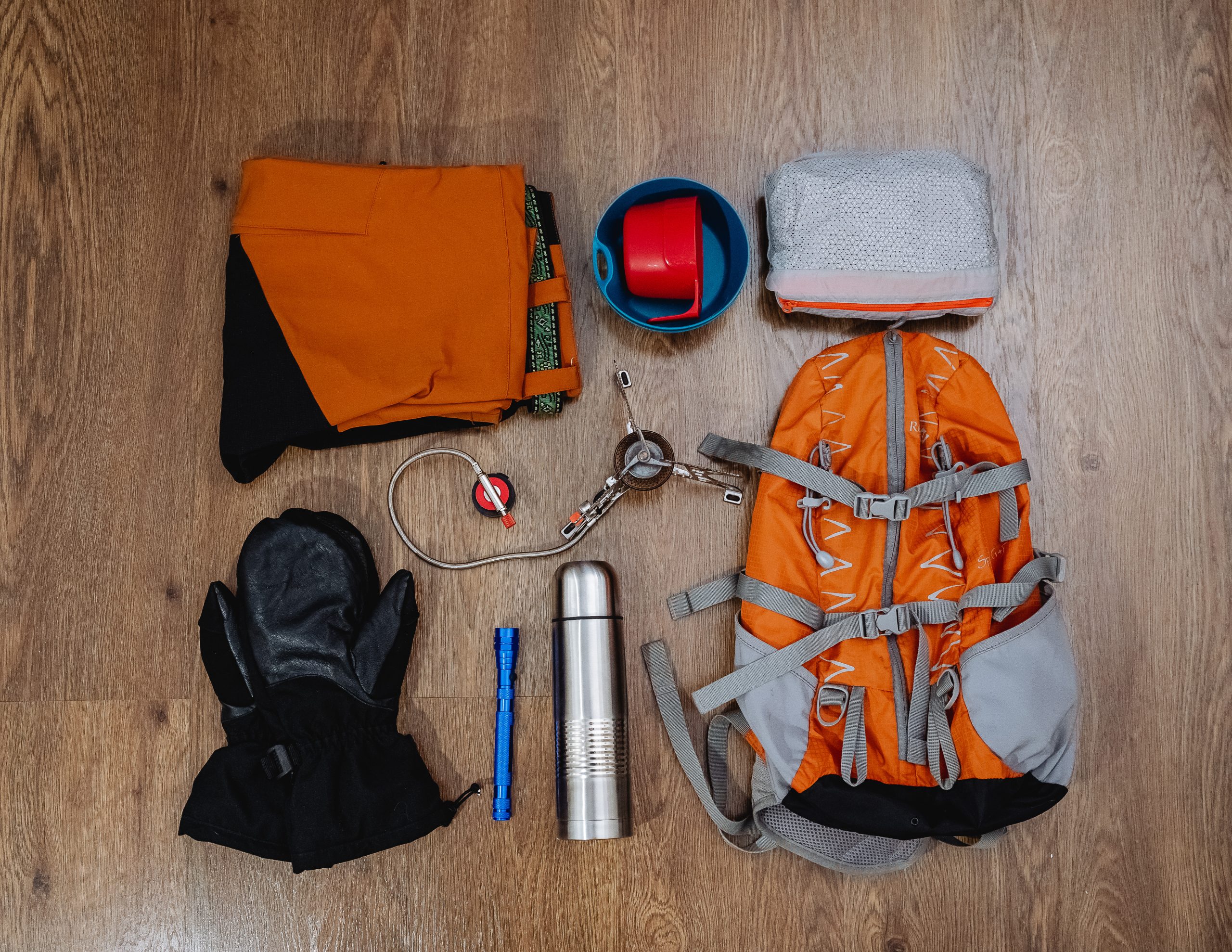 Hiking equipment, backpack, pants, thermos, mittens, lantern, windbreaker lie on the floor.