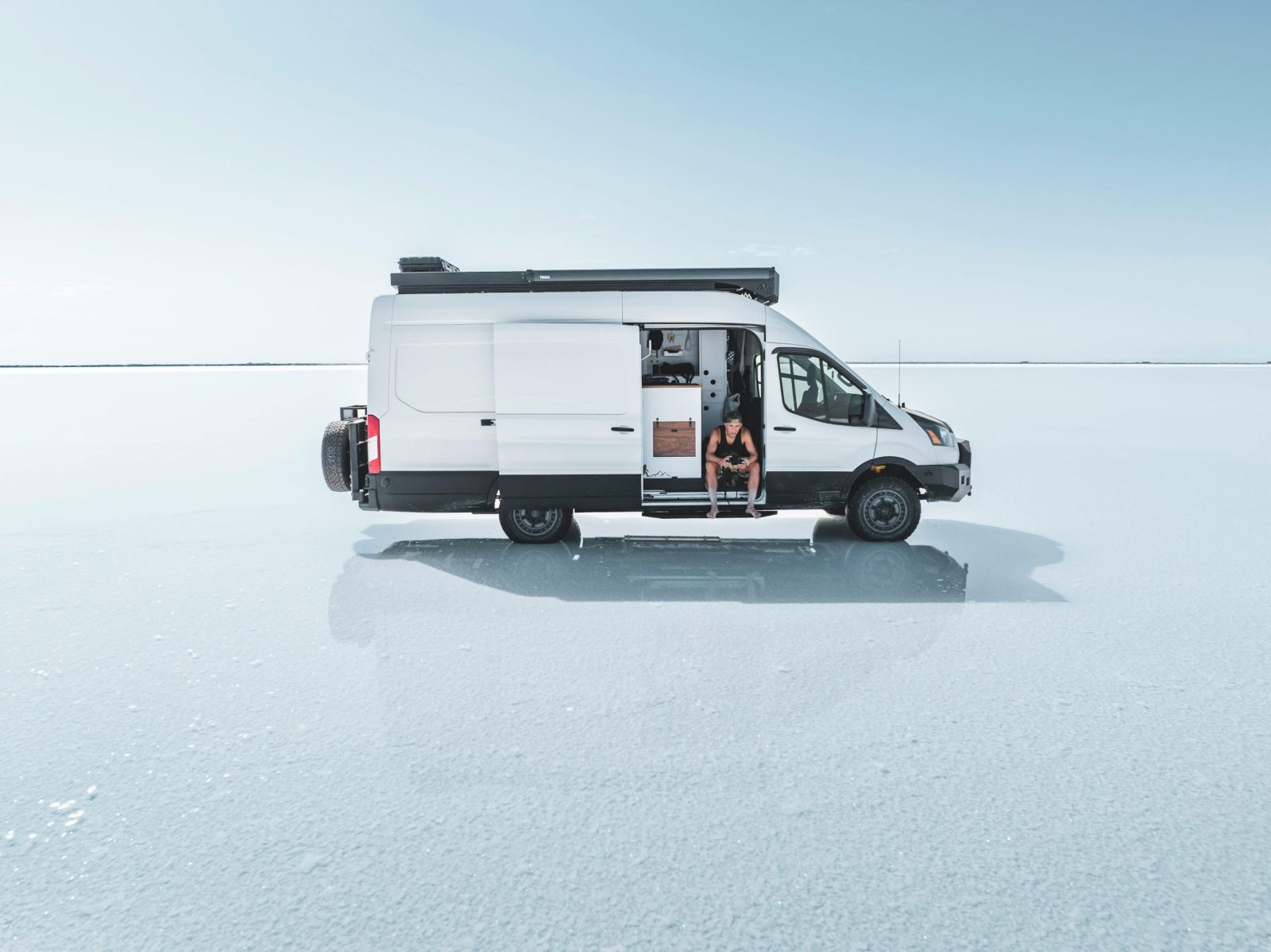 Camper van parked on a vast, open salt flat under a clear sky.
