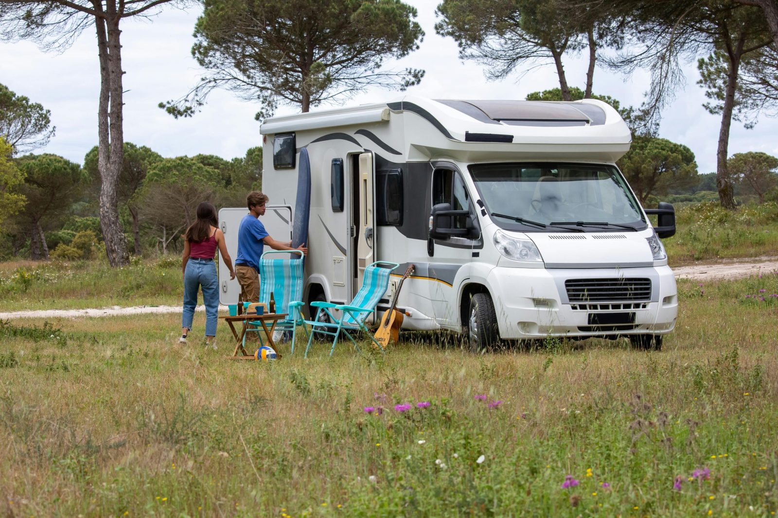 A couple enjoys a camping trip with their RV in a scenic grassland, surrounded by nature.