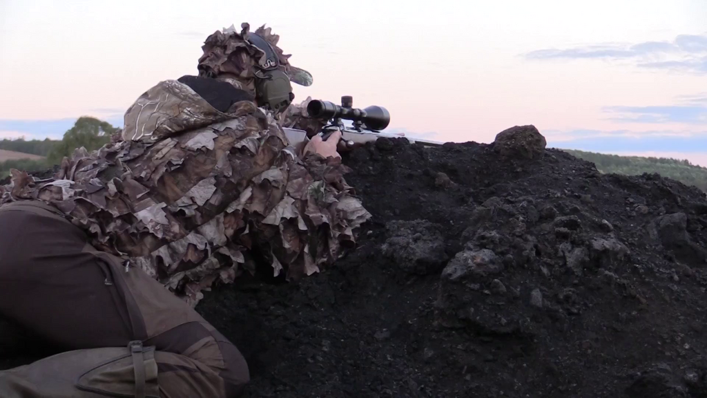 A Hunter Sitting Behind a Rock and Wearing Ghillie Suit