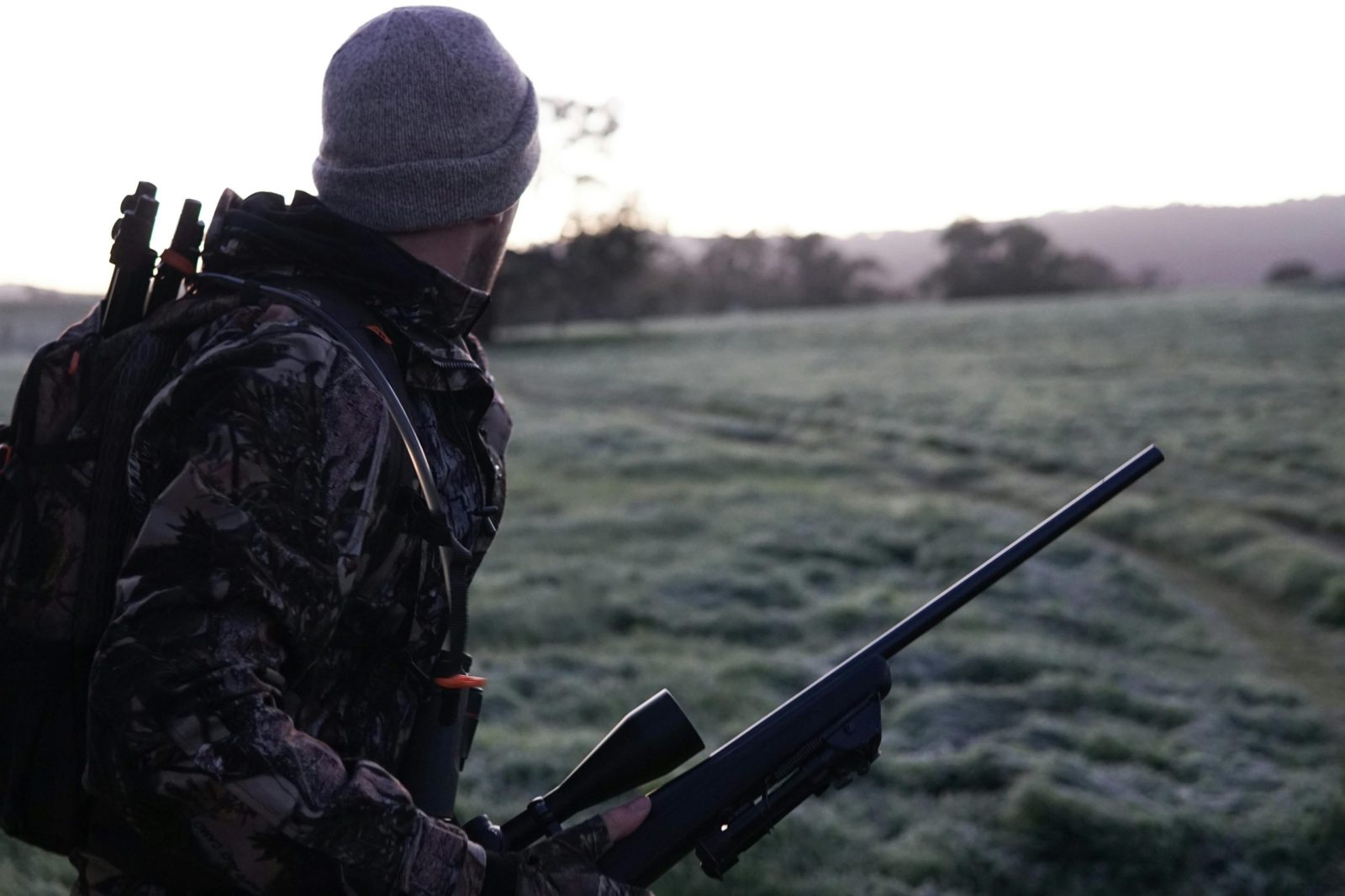 Camouflaged hunter surveying the landscape with rifle at dawn in Victoria, Australia.