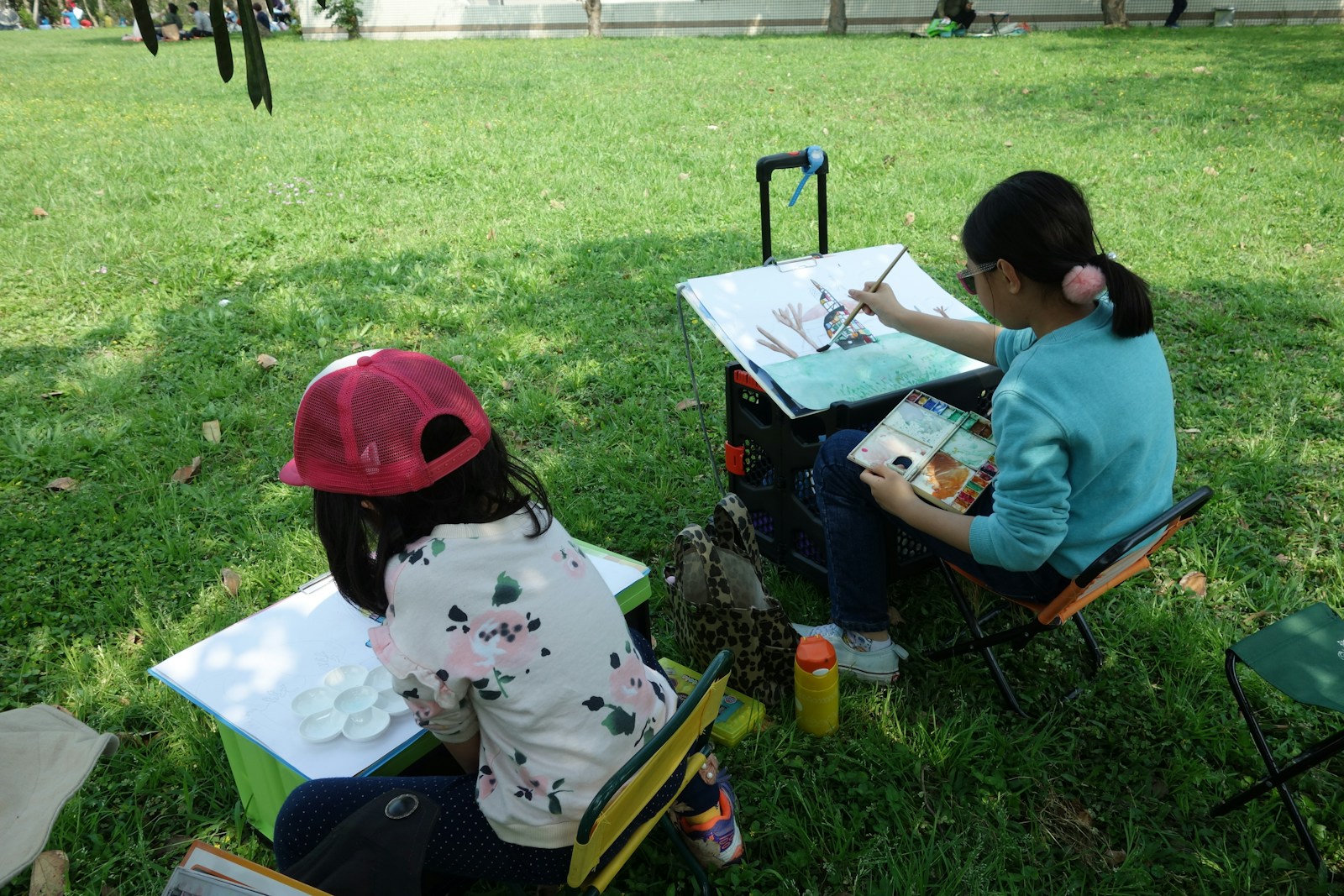 A couple of kids that are sitting in the grass and painting
