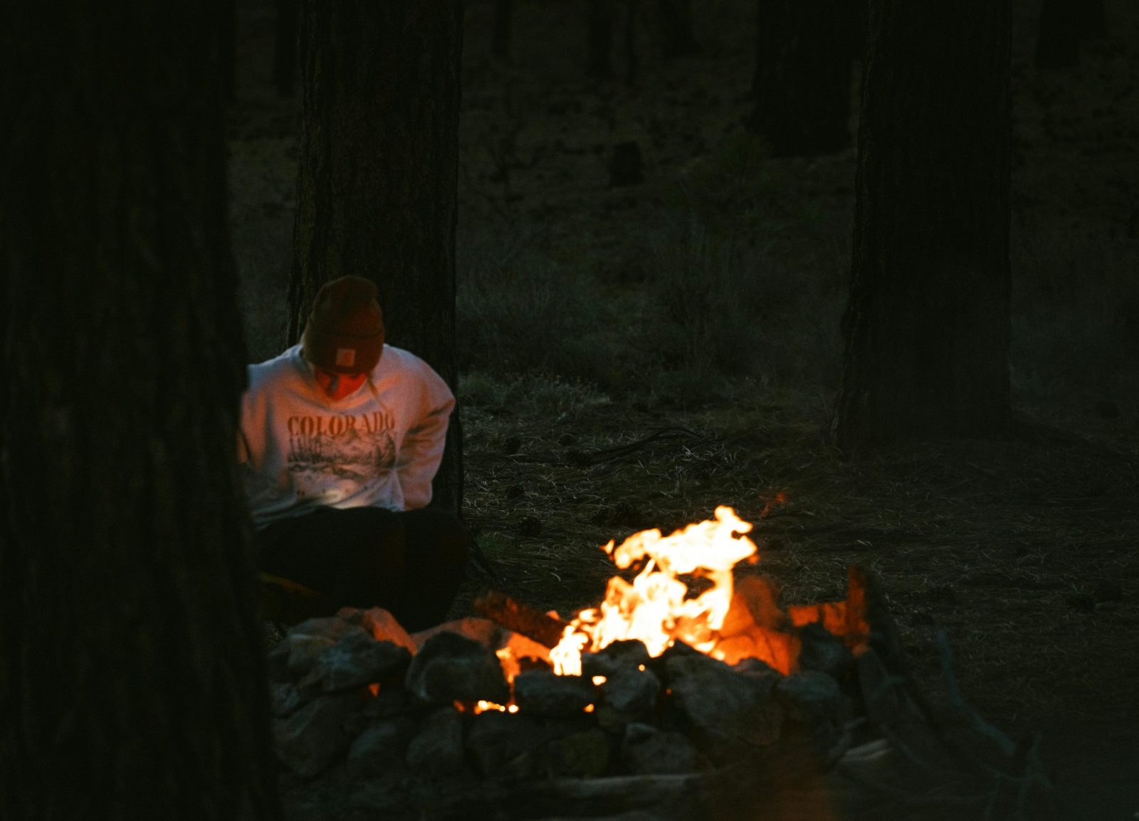 A person sits by a campfire in the forests of Utah, creating a cozy nighttime atmosphere.