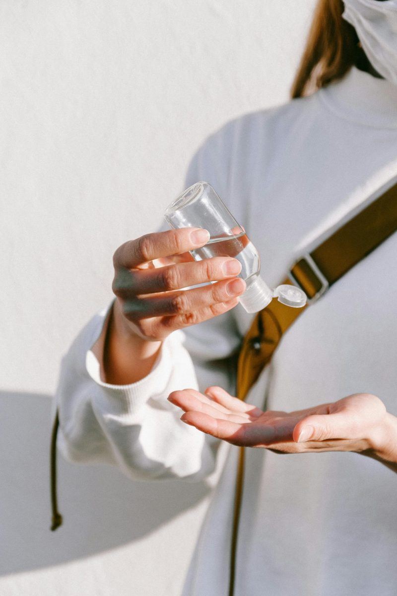 Close-up of a woman using hand sanitizer with a white background, emphasizing hygiene.
