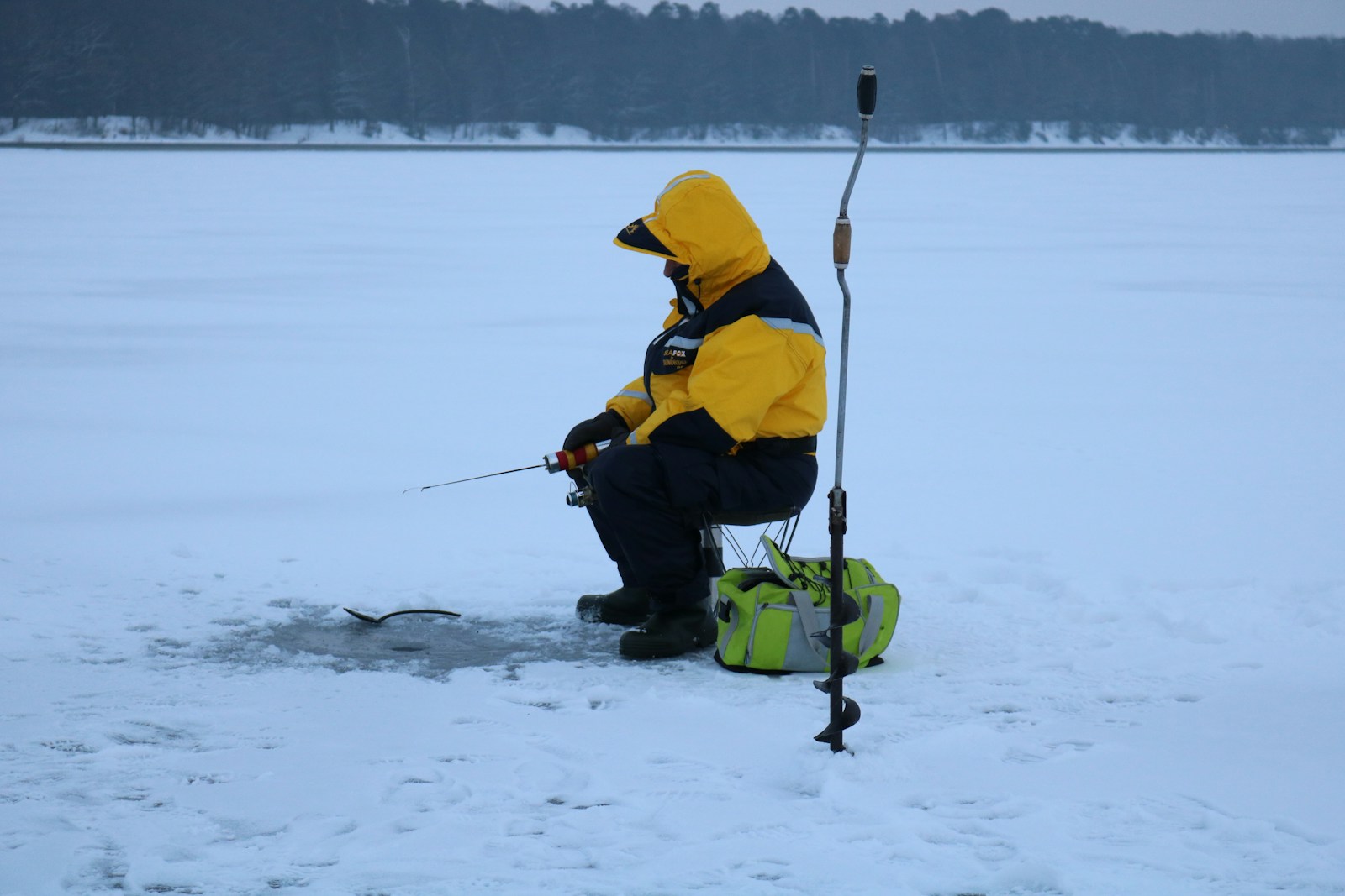 A man in a yellow jacket fishing on a frozen lake