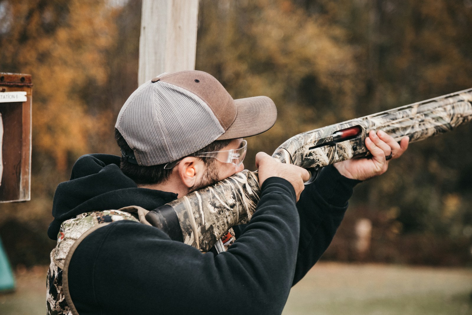 A man with a hat and glasses aims a rifle