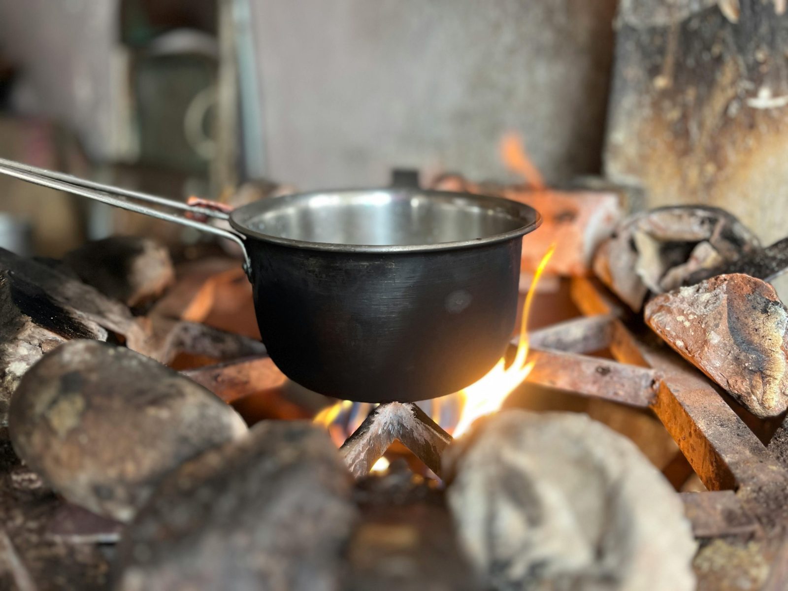 Metal pot on open fire cooking setup, rustic and traditional kitchen scene.
