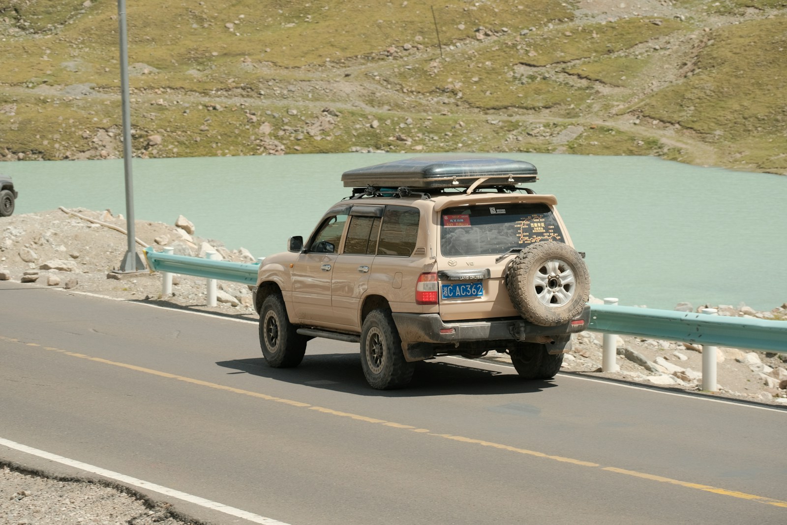 Suv drives down a road next to a lake.