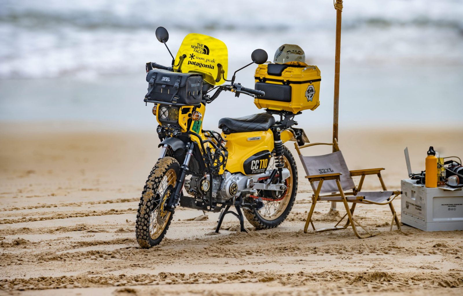 Adventure motorcycle parked on sandy beach with camping gear setup.