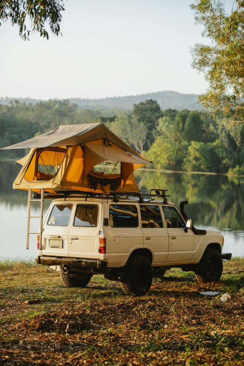 Explore the tranquil lakeside campsite with a car and rooftop tent, perfect for summer adventures.