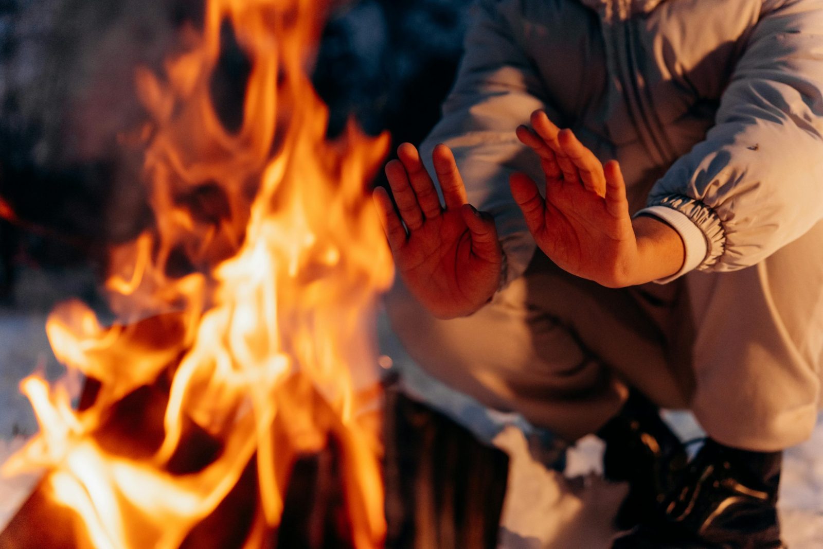 Close-up of hands being warmed by a campfire at night during winter, showcasing warmth and comfort.