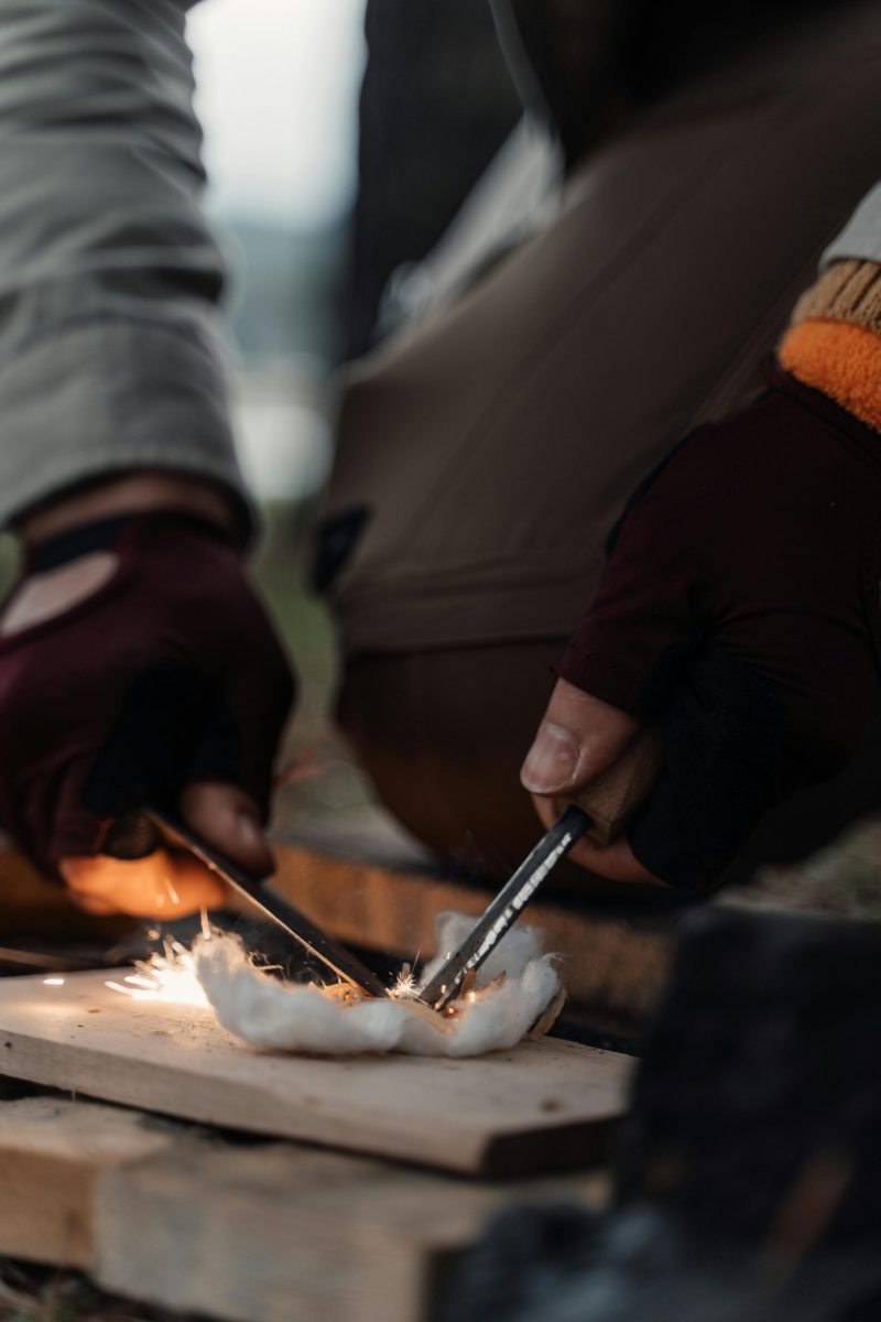 Close-up of a man using flint and steel to start a fire outdoors, showcasing survival skills.
