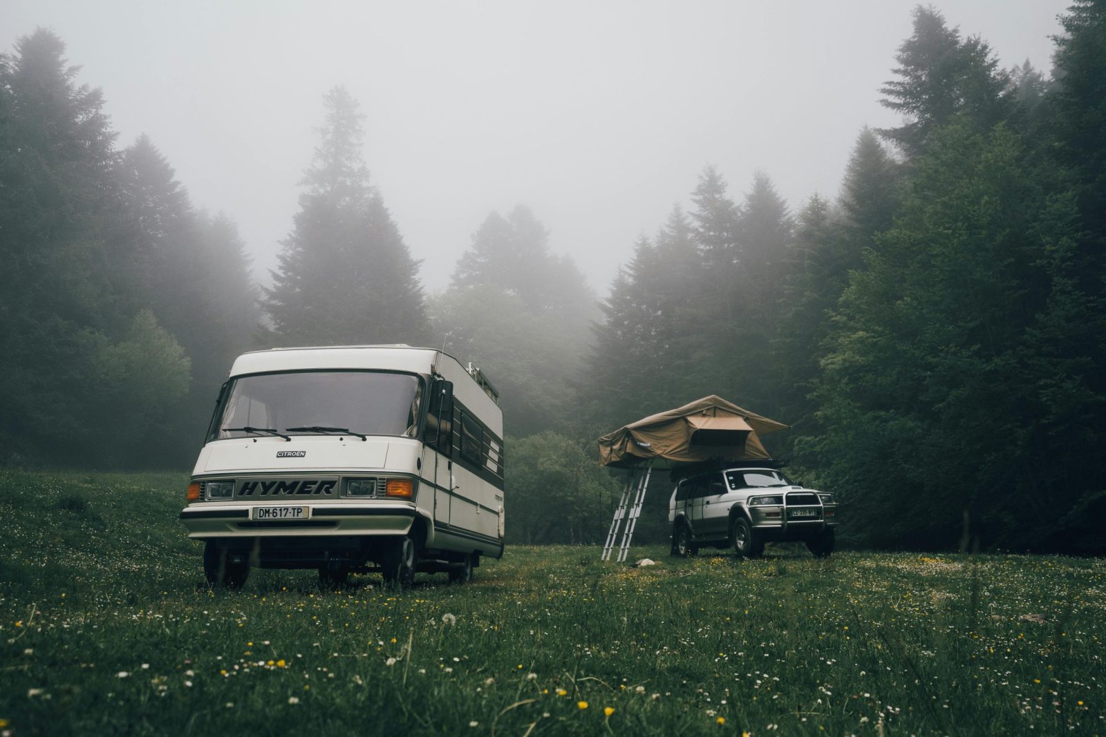 Scenic view of RV and tent in a foggy forest meadow, perfect for adventurous campers.