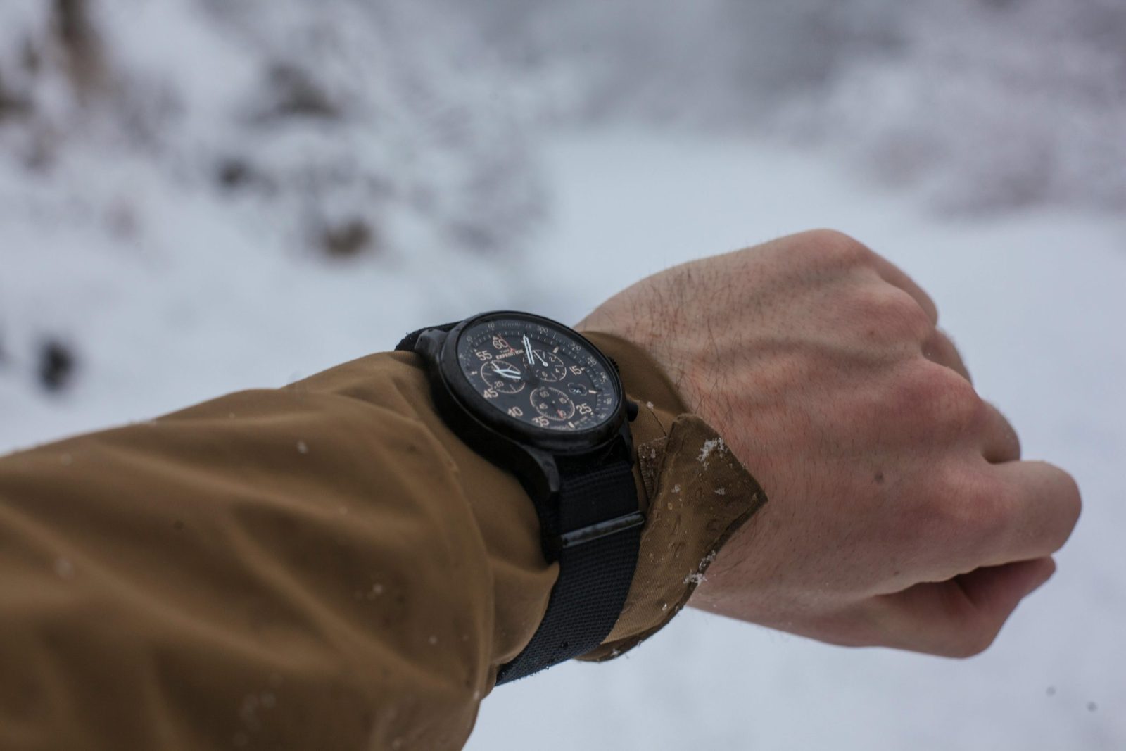 Man checks time on wristwatch outdoors, surrounded by snowy scenery for wintertime adventure.