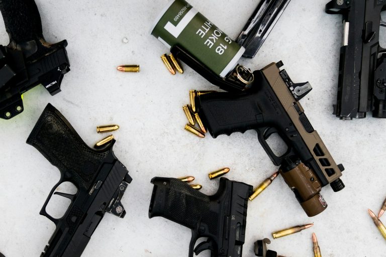 A mix of sig and glocks pistols sitting on a table along with a smoke grenade and some bullets.