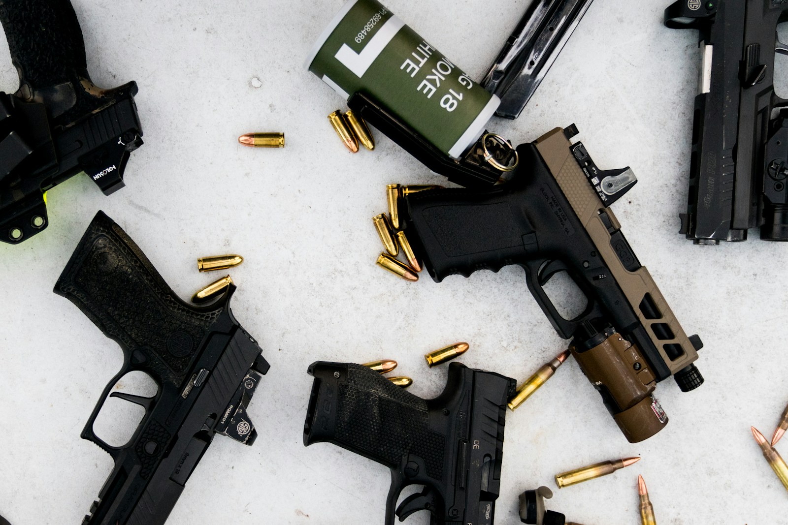 taiki-ishikawa-w6EMxsk8CDA-unsplash A mix of sig and glocks pistols sitting on a table along with a smoke grenade and some bullets.