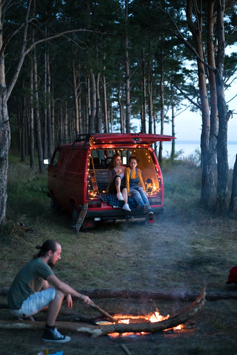 A Man Sitting Near the Bonfire while the Two Girls Sitting on the Van