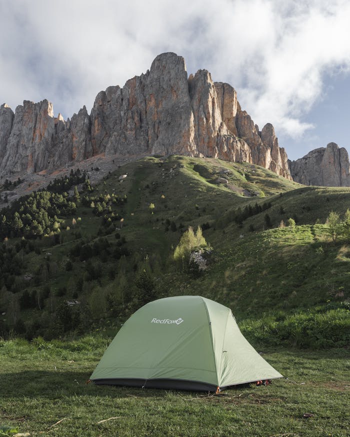 Green Tent Standing in Mountain Meadow in Front of Rocky Ridge