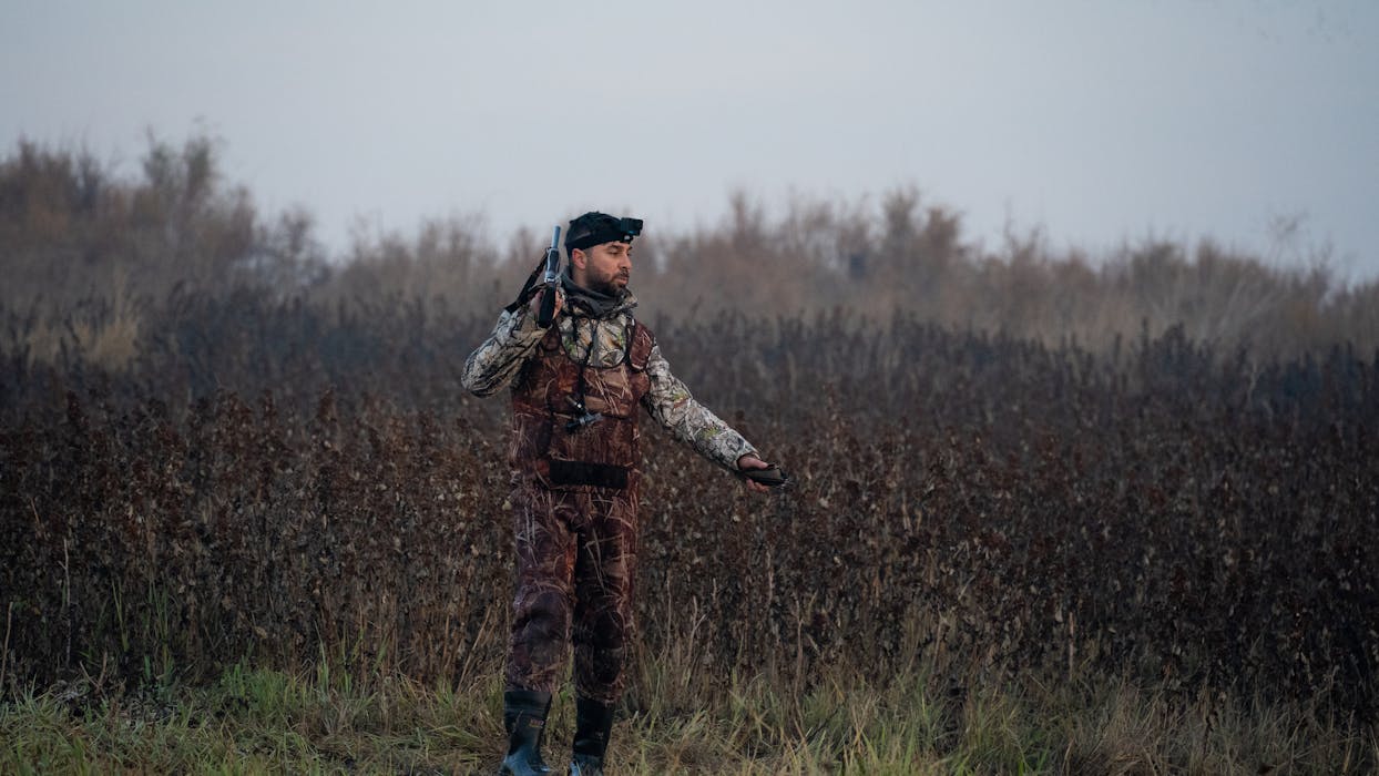 Hunter in Camouflage Jacket Standing on a Field