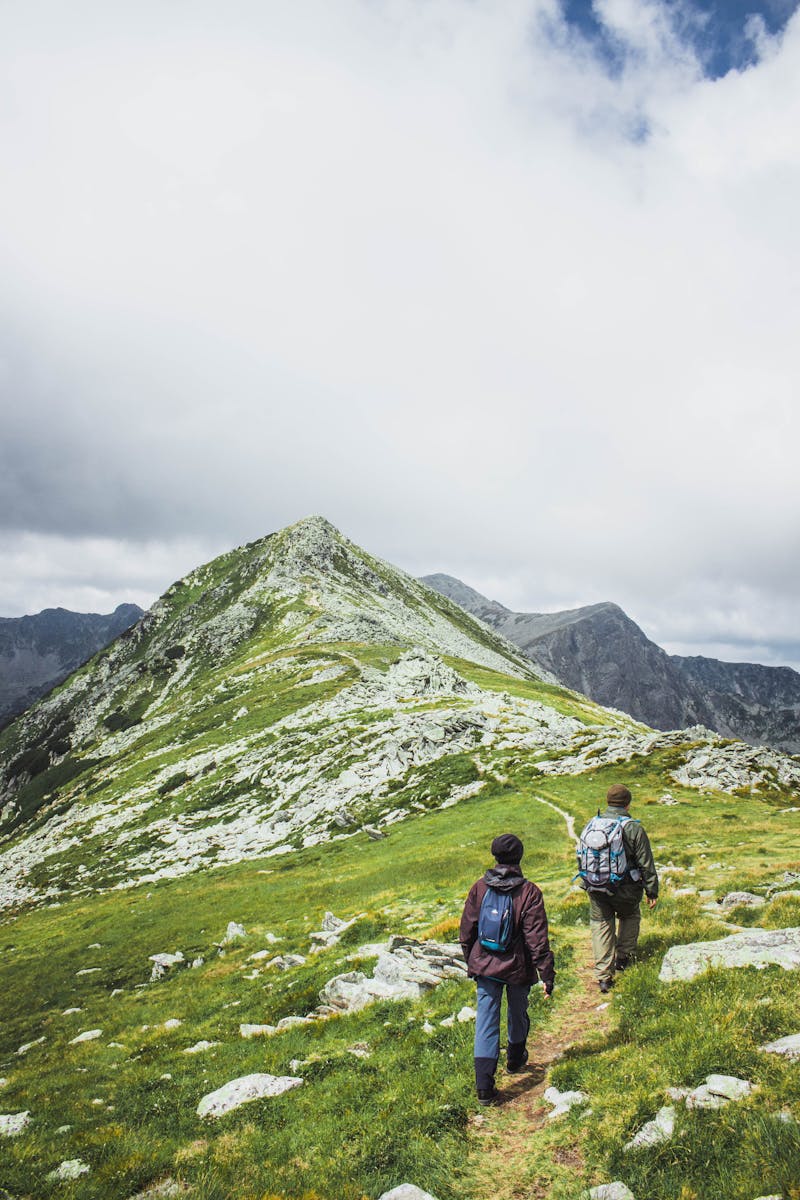 Two Men Walking on a Hill Under White Clouds
