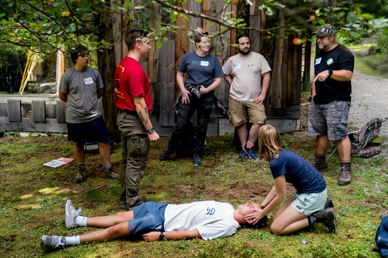 People practicing cpr outdoors under trees.