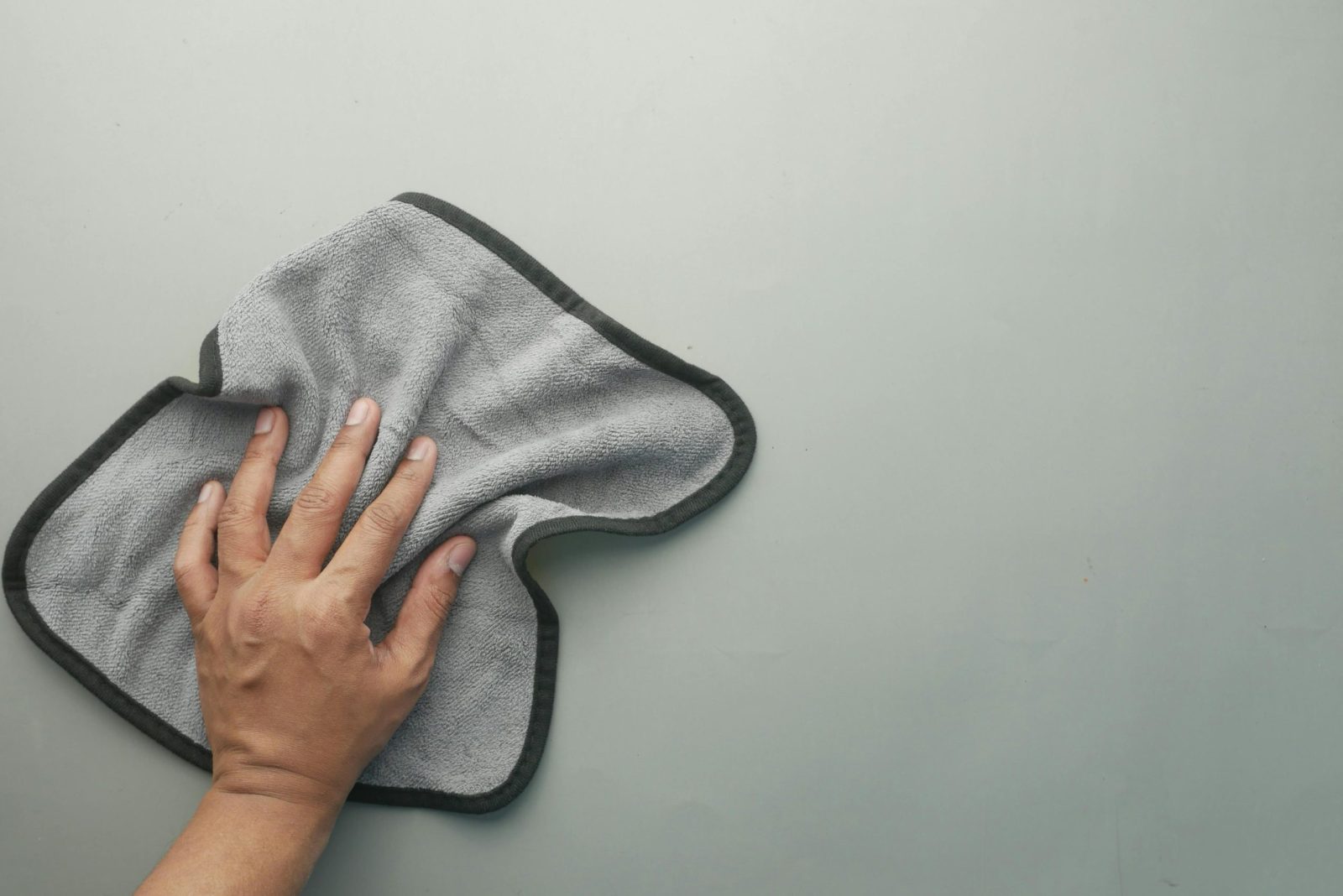 A hand wipes a light-colored table using a gray microfiber cloth, ideal for cleaning concepts.