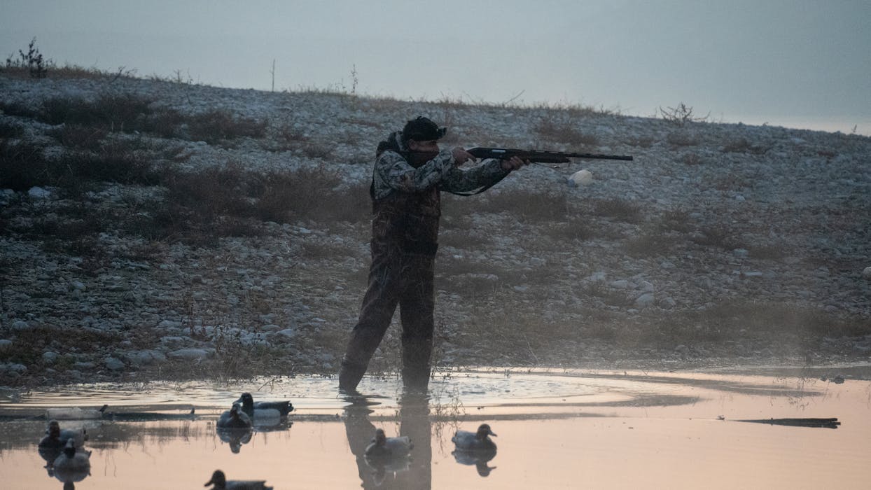 Hunter with Rifle Moving through Muddy Water