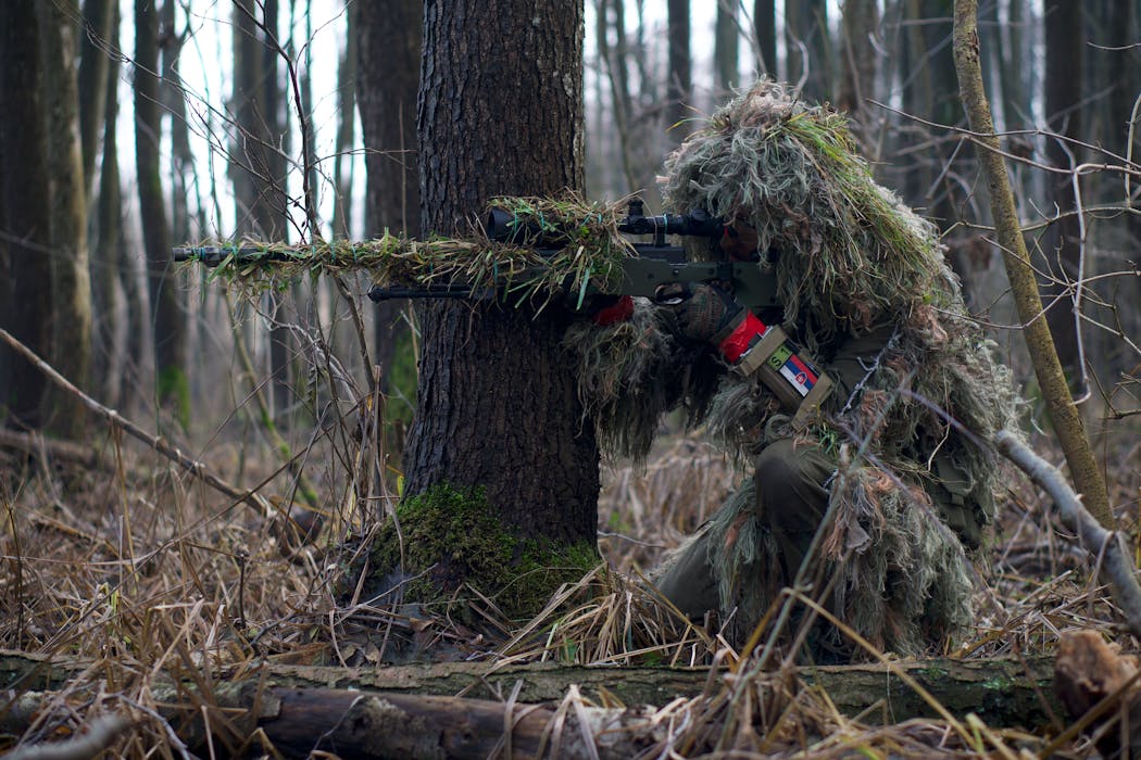 A Sniper Aiming Though The Rifle Scope In Forest