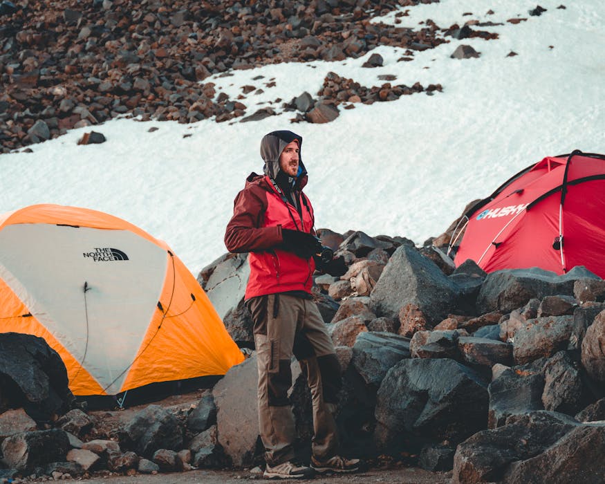 Man in Red Jacket Standing next to Camp