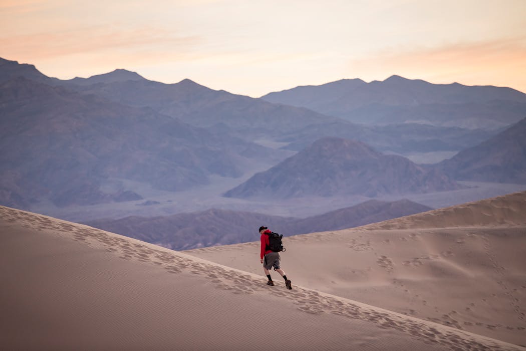 Hiker in Red Ascending Desert Dune at Sunrise