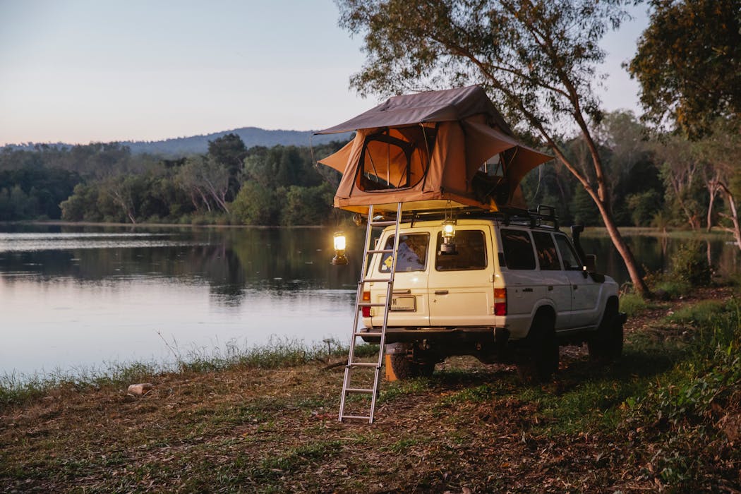 taiki-ishikawa-w6EMxsk8CDA-unsplash SUV car with camping tent parked on lake coast in woods during road trip