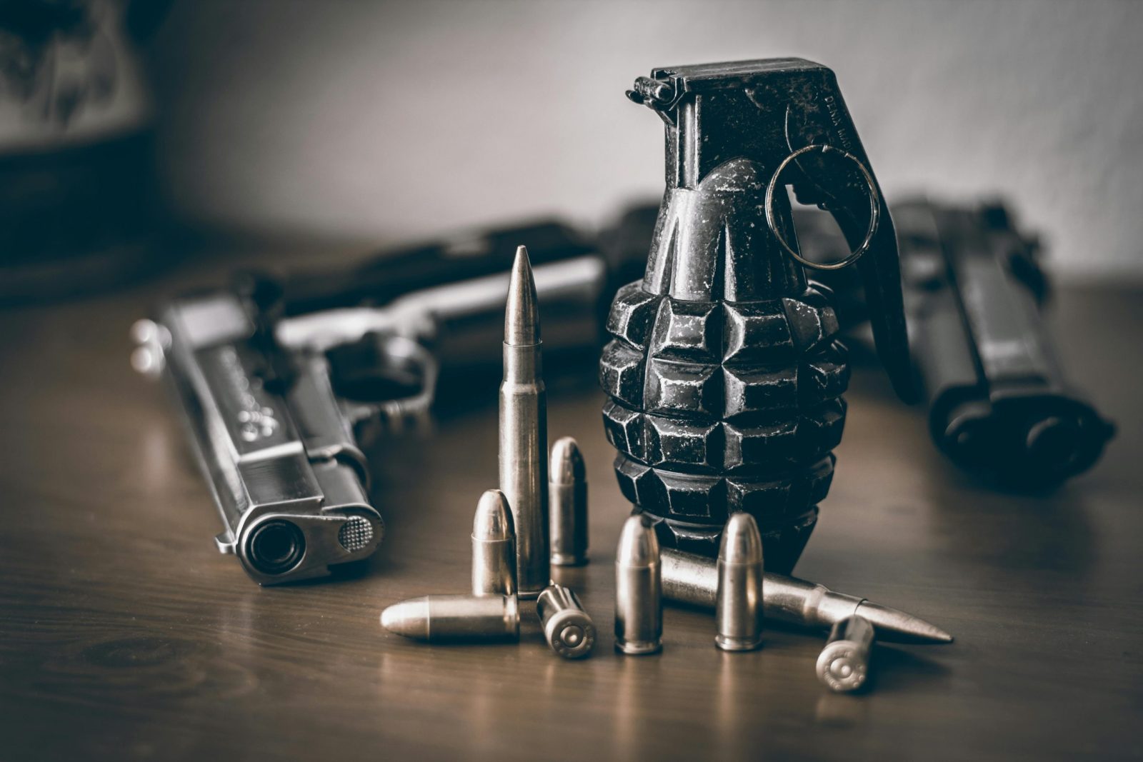 A collection of weapons including a pistol, grenade, and bullets on a wooden surface.