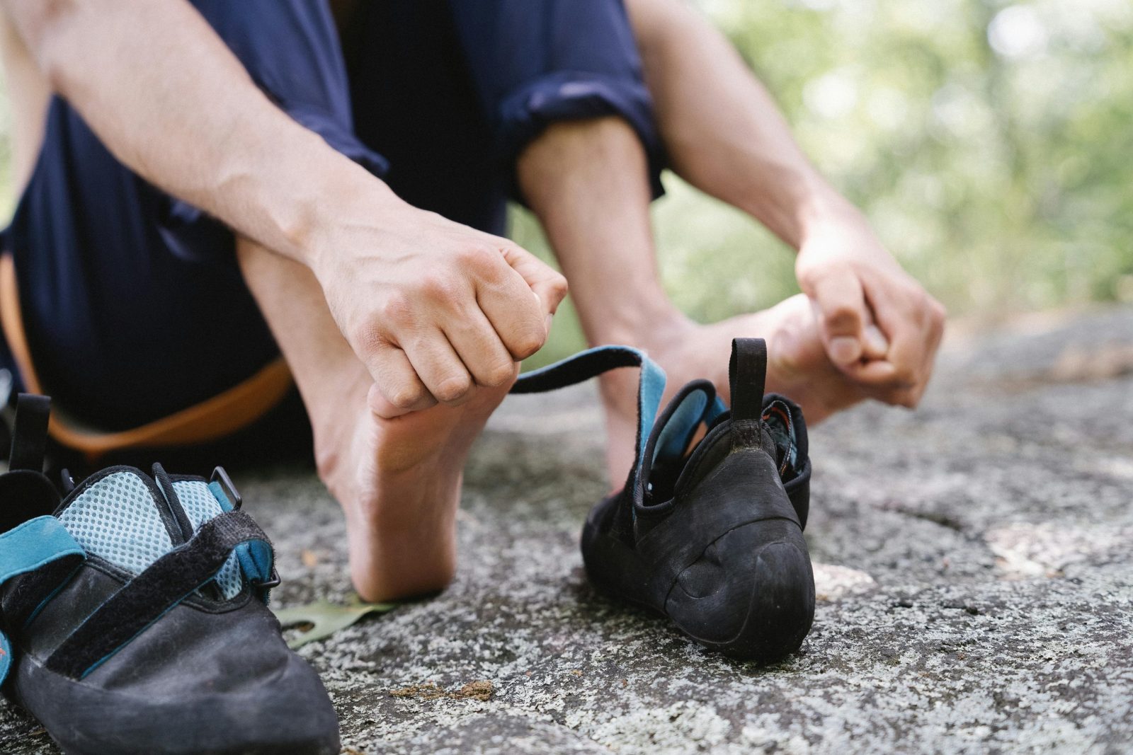 Person sitting on rock adjusting climbing shoes, showcasing outdoor adventure and preparation.